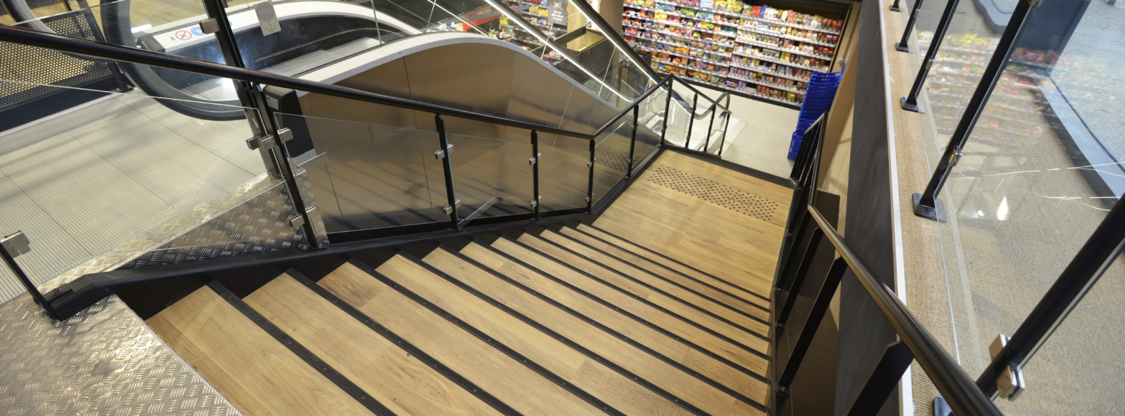 Vue dessus escalier conforme normes ERP supermarche escalier acier noir garde-corps verre et marches linoleum.